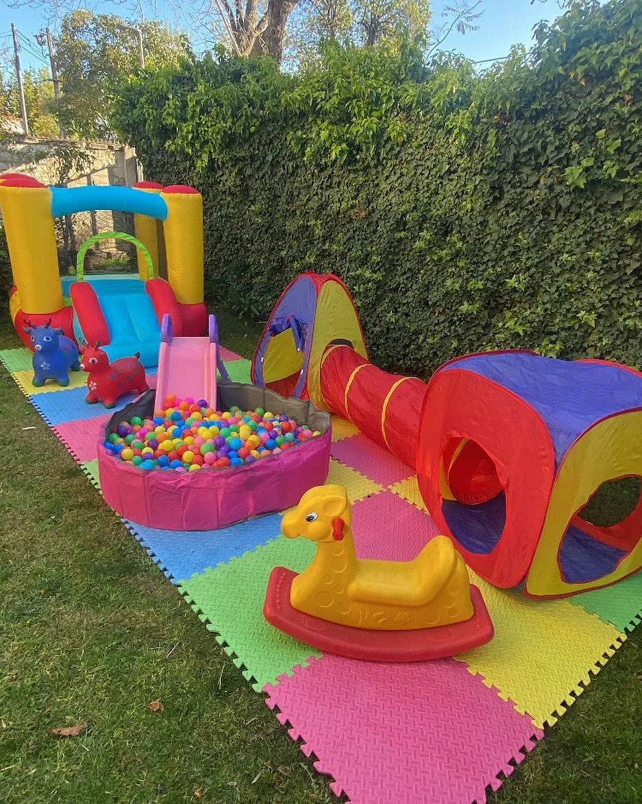 Plaza Blanda montada contra un muro de hiedra: inflable dorado, resbalín, piscina de pelotas y piso blando