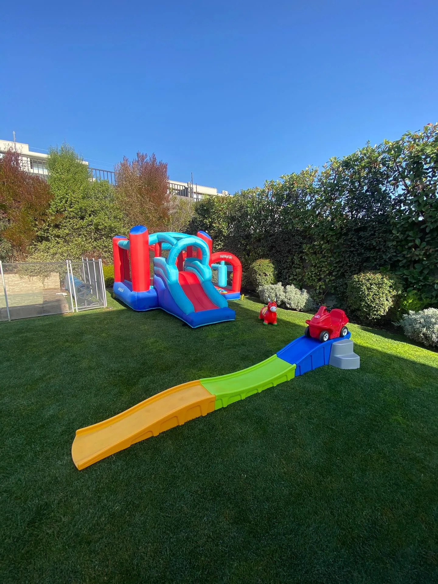 Inflable con resbalín largo y pista de autos correpasillos en un jardín amplio