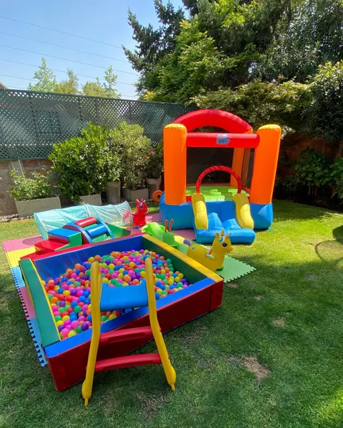 Plaza Alegría montada en un jardín arbolado: inflable naranjo, piscina de pelotas y resbalín