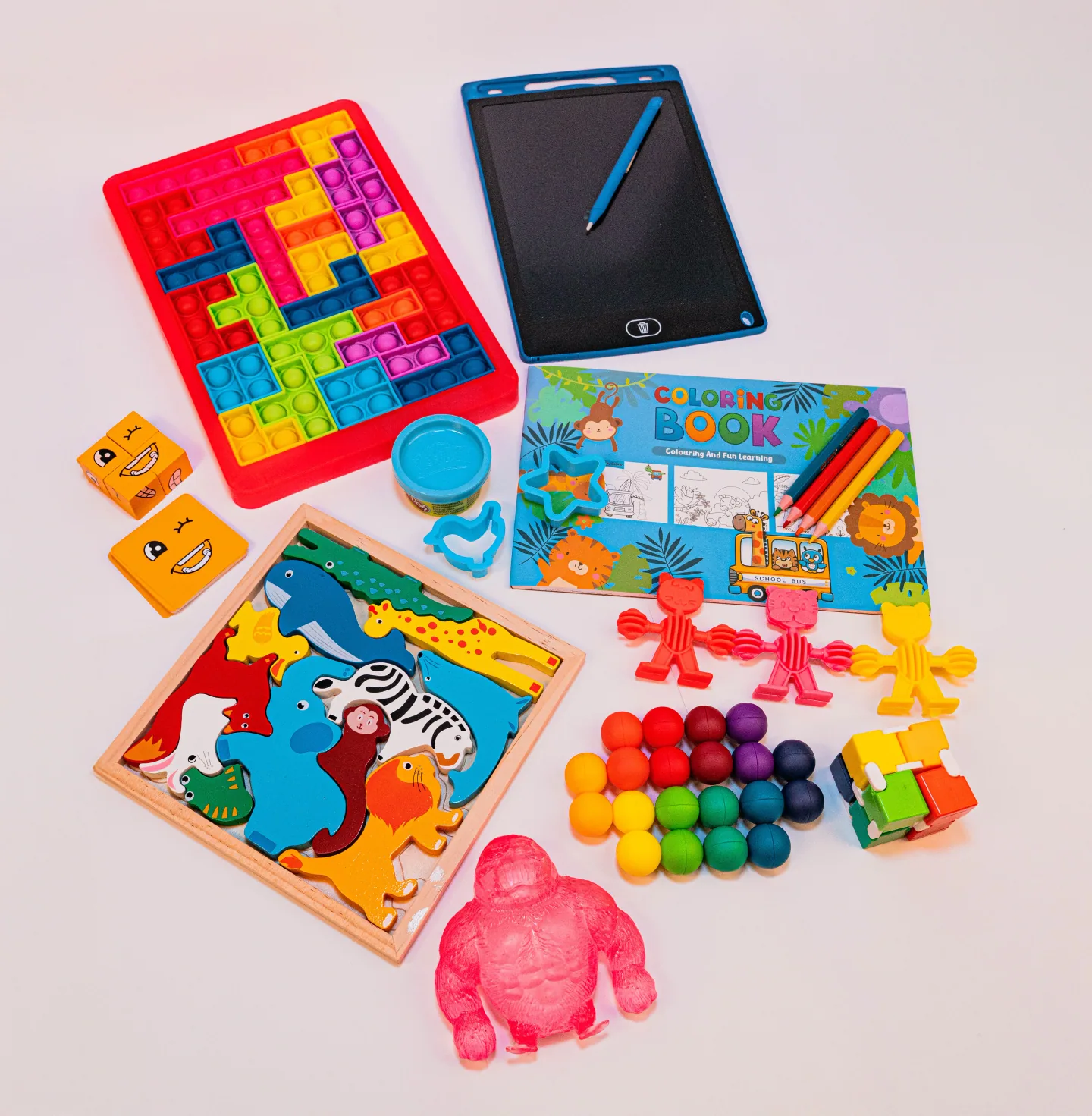 Los 8 juguetes del Play Kit desplegados sobre fondo crema: pizarra mágica, libro para colorear, imanes, puzzle de caritas, masa con cortadores, jirafa extensible y capibara