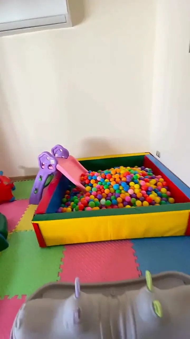 Piscina de pelotas llena de pelotas de colores con resbalín lila, recién montada dentro de una casa